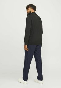 Schwarzer Pullover mit hohem Kragen, kombiniert mit navyfarbener Hose. Der Pullover hat lange Ärmel und eine glatte Textur, während die Hose tailliert ist.
