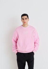 Růžová mikina s vyšitým logem "GAP", kulatý výstřih, uvolněný střih, žebrované manžety, v kombinaci s černými kalhotami.