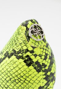 Sac en fausse peau de serpent noir et jaune fluo ; présente un accent de logo métallique et un motif reptilien texturé ; forme arrondie sur le dessus.