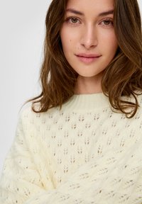 Helles gelbes Strickpullover mit einem Blattmuster, geripptem Rundhalsausschnitt und weicher Textur. Betont Drapierung und Lagen-Design.