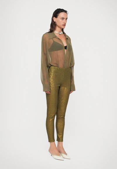 Priesvitná olivovo zelená blúzka, čierny top pod ňou, legíny s zlatými flitrami, biele špicaté baleríny a perlový náhrdelník.