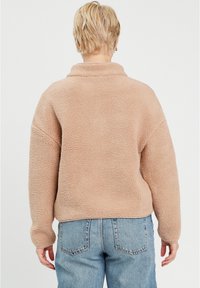 Pull en polar beige avec une texture douce et duveteuse, col large et épaules tombantes, associé à un jean en denim bleu clair.