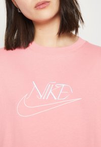 Růžová bavlněná mikina s výšivkou bílého loga Nike. Design zahrnuje kulatý výstřih a krátké rukávy.