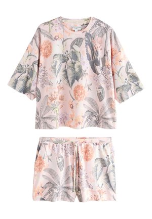 Vrouw met bruin haar in een paardenstaart draagt een losse top met bloemenprint en bijpassende shorts in zachte roze, grijze en beige tinten, staand zijwaarts.