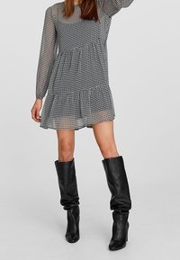 Vestido a rayas en blanco y negro con mangas largas, diseño en capas y tejido ligero. Combinado con botas altas de cuero negro con caída.