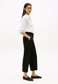 Witte overhemd met opgerolde mouwen, zwarte op maat gemaakte broek met zakken en zwarte instappers. Eenvoudige, strakke lijnen en klassieke kleuren.
