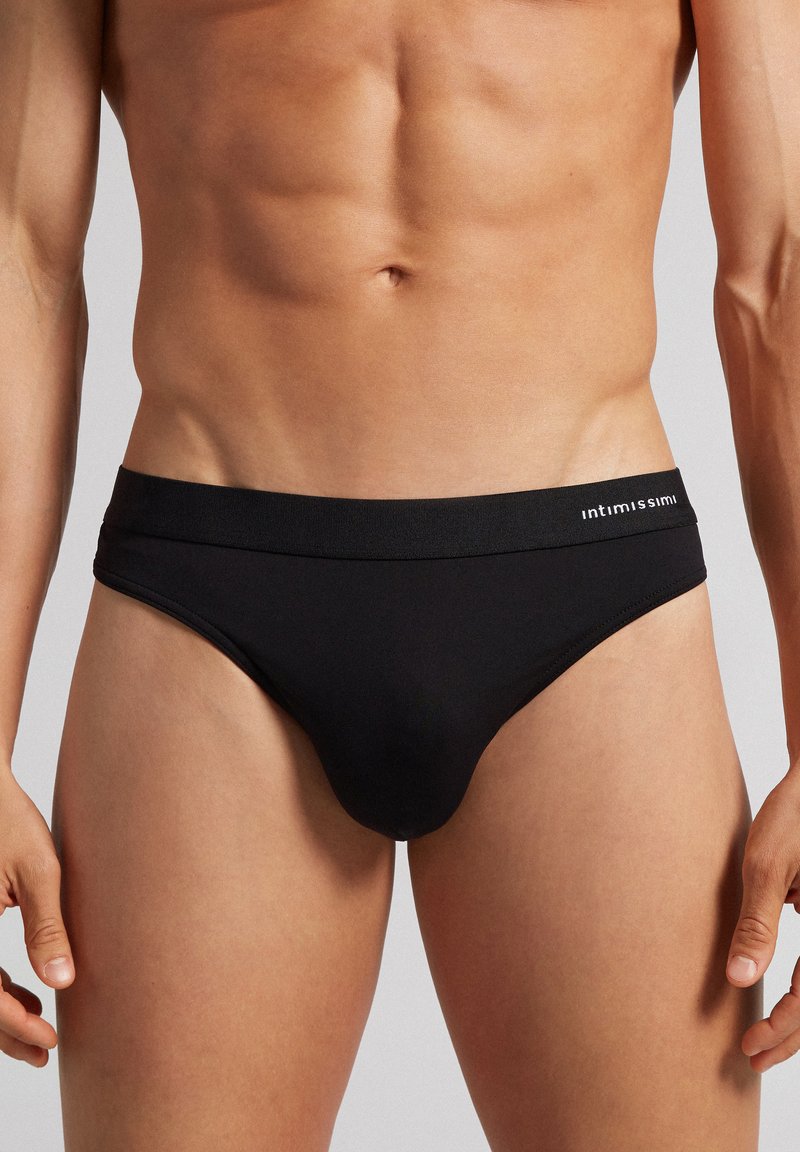 Boxers noirs pour hommes en tissu lisse, dotés d'une large ceinture avec une marque blanche, d'une forme ajustée et d'un design épuré.