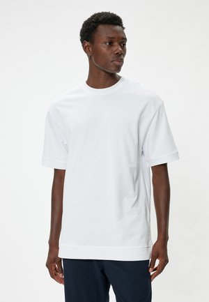 Camiseta blanca de algodón de manga corta con cuello redondeado y hombros caídos, que presenta un corte relajado y un dobladillo recto.
