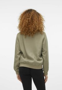 Oliwkowa bluza z długim rękawem, ściągacze przy mankietach i u dołu, gładka tekstura oraz luźny krój; noszona z czarnymi legginsami.