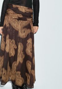 Gonna marrone con motivo, realizzata in tessuto fluido, con accenti metallici dorati, disegni intricati e una vita arricciata.