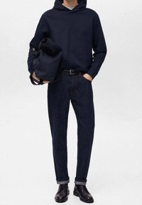Granatowa bluza z kapturem, ciemne dżinsy i czarne skórzane buty. Torba w ręku, o gładkiej fakturze. Rękawy spodni podwinięte z klasycznym krojem.