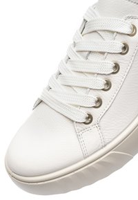 Nærbillede af hvid lædersneaker med afrundet tå, tykke hvide snørebånd trukket gennem sølvfarvede snørehuller og tekstureret sålkant.