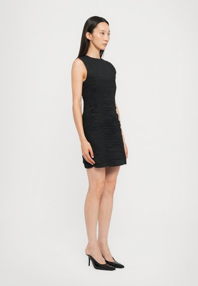 Black sleeveless dress with gathered texture, featuring a fitted silhouette and a knee-length hem. Paired with black high-heeled shoes.