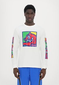 Langärmliges weißes T-Shirt mit einem bunten Grafikdruck eines roten cartoonartigen Gesichts auf der Vorderseite und kleineren Versionen an den Ärmeln.