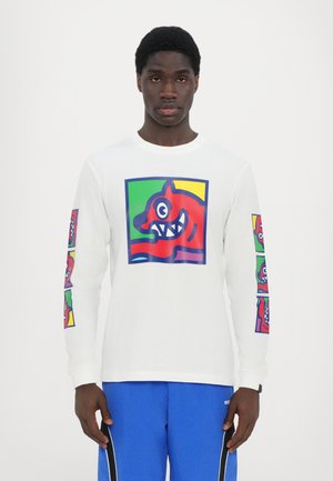 T-shirt à manches longues blanc présentant un graphisme coloré d'un visage de dessin animé rouge sur le devant et des versions plus petites sur les manches.