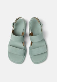 Kaksi mintunvihreää sandaalia, joilla on moderni muotoilu, leveillä mokkanahkaisten hihnojen, säädettävän nilkkapainikkeen ja teksturoidun pohjan kanssa.
