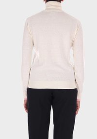 Maglione a collo alto color crema realizzato in materiale knit morbido, con un design aderente e polsi e orlo ribattuti; indossato con pantaloni neri.
