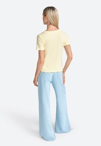 Top giallo a maniche corte con coste e bordi scallop, abbinato a jeans a gamba larga blu chiaro con tasche posteriori e una vestibilità rilassata.