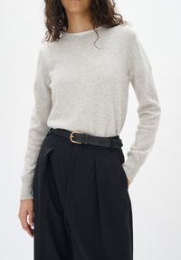 Maglione grigio chiaro realizzato in materiale morbido, con scollatura rotonda e maniche lunghe, abbinato a pantaloni neri a vita alta e una cintura nera.