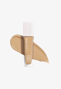 Fond de teint Lancôme Teint Idole Ultra Wear dans un flacon en verre transparent avec un capuchon blanc ; présente un échantillon de liquide beige crémeux à côté.