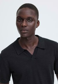 Polo noir en maille avec un col en V, manches courtes et col texturé. Tissu lisse sans motifs ni accents.