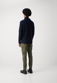Marineblauer Strickpullover mit Kragen, olivgrüne Cargo-Hosen und schwarze Stiefel. Kleidung von hinten vor einem schlichten Hintergrund gezeigt.