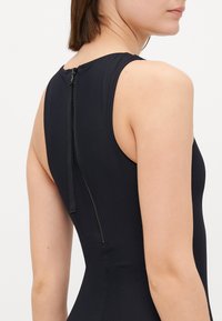 Bodysuit sans manches noir avec un col montant, une texture lisse et une fermeture à glissière au dos avec un tirette en tissu.
