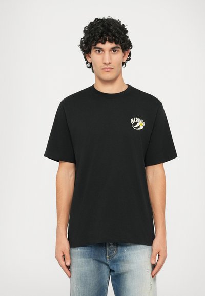 Juodas medvilninis marškinėliai su trumpomis rankovėmis, pažymėti mažu grafiniu piešiniu su tekstu ir animaciniais akcentais kairėje krūtinės pusėje.