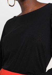 Mustat yläosat, joissa on hieman olkaimia paljastava muotoilu, sileä pinta ja löysä istuvuus; varustettu laskostetuilla hihoilla ja yhdistetty punaisiin alaosiin.