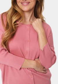 Pink cardigan featuring ribbed texture, crew neckline, and five buttons. Elbow-length sleeves and relaxed fit showcase a soft, comfortable design.