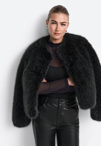 Jachetă din blană sintetică neagră cu un guler larg, asortată cu un top transparent negru și pantaloni din piele ajustați. Textură elegantă și design voluminos.