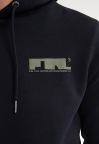 Sudadera marina de tejido suave que presenta un destacado logo verde con el texto "PTRL PETROL INDUSTRIES NORTHWOODS WISCONSIN U.S.A."