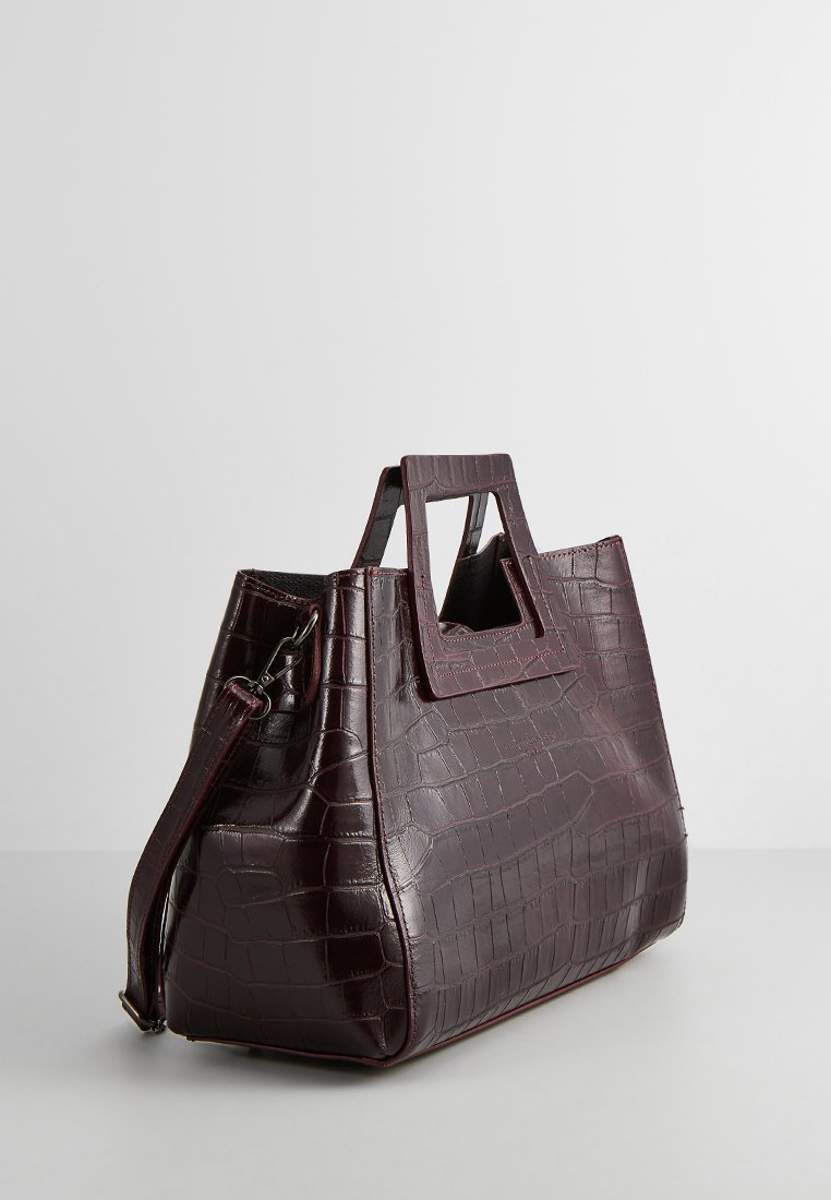 Borsa a mano in pelle con stampa a coccodrillo di colore marrone scuro, dotata di manici rettangolari e tracolla attaccata, su uno sfondo neutro.