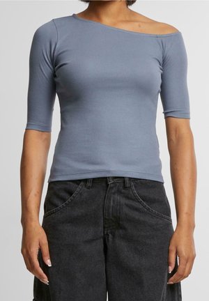 Kvinde iført en tætsiddende, off-shoulder, lyseblå ribbet top med halværmer og højtaljede løse sorte denim jeans.