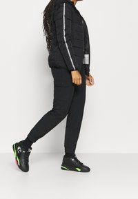 Black puffer jacket with a hood and silver stripe accents, paired with black cargo pants and black sneakers featuring green and pink details.