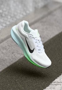 Λευκό αθλητικό παπούτσι με άνω μέρος από διχτυωτό υλικό, μαύρο λογότυπο Swoosh και πράσινη λεπτομέρεια στη σόλα. Διαθέτει κορδόνια και πρεσαριστή υφή για καλύτερη διαπνοή.