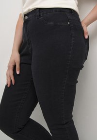 Jeans en denim noir au design ajusté, présentant un style classique à cinq poches et des détails de couture subtils aux coutures.