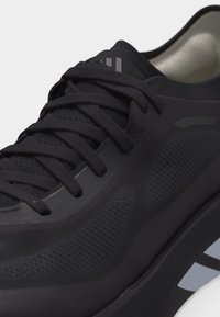 Chaussure de sport noire avec tige en mesh texturé, fermeture à lacets, intérieur rembourré et logo Adidas sur la languette et la semelle.