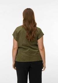 Haut vert olive à manches courtes avec une texture douce et lisse. Il présente une coupe décontractée, des détails au niveau du col, et est associé à un pantalon noir.