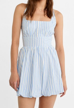 Vrouw die een mouwloze jurk draagt met verticale blauw-witte strepen, een vierkante halslijn en een geplooide rok.