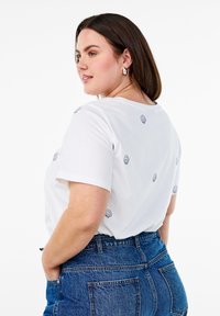 White cotton t-shirt featuring small navy embroidered shell designs, short sleeves, and a relaxed fit, paired with high-waisted denim shorts.