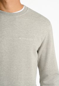 Grå sweatshirt i mjukt tyg med rund halsringning, som har en diskret vit "JUNK de LUXE" logotyp på bröstet.