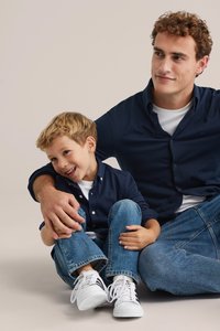 Jūras flotes pogājamā krekla uz zēna, baltā T-kreklā uz vīrieša, džinsu biksēs un abiem baltās sporta apavos. Mīksts, neitrāls fons.