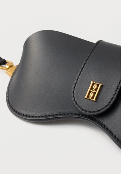 Μαύρο δερμάτινο θήκη με καμπυλωτό σχήμα, λεπτομερείς ραφές, χρυσό κούμπωμα και μικρό χρυσό έμβλημα στην μπροστινή πλευρά.