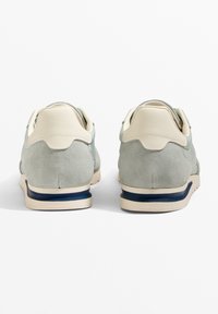 Sneaker aus heller grüner Wildleder mit cremefarbenen Lederakzenten. Sie verfügen über eine beige Sohle mit einem blauen Streifen. Abgerundetes, gepolstertes Design.