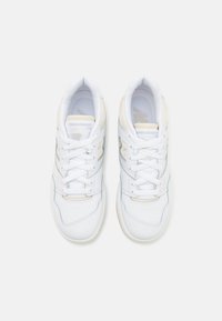 Paire de baskets blanches New Balance avec des accents beige clair et des lacets blancs, vue de dessus sur fond blanc.