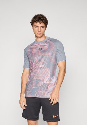 Maglietta sportiva grigia con un motivo astratto rosso, maniche corte, scollatura rotonda e dettagli blu. Abbinata a pantaloni corti scuri con un logo.
