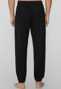 Schwarze Stretchhose mit einem elastischen Bund, die ein tailliertes Bein-Design und Bündchen an den Knöcheln aufweist. Glatte Textur, keine Muster oder Verzierungen.