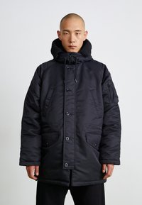 Schwarze gepolsterte Parka mit Kapuze, ausgestattet mit Druckknöpfen, zwei Fronttaschen und einem strukturierten Kragen. Hergestellt aus glattem, isoliertem Stoff.