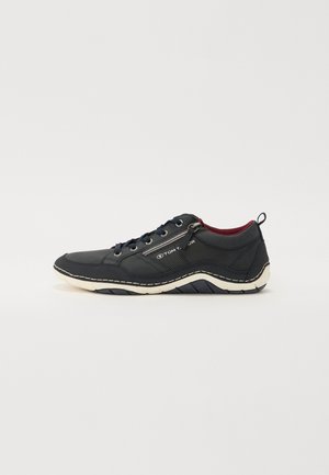 Navy sneaker with a textured fabric upper, contrasting white sole, lace-up front, and side zipper detail. Features logo branding on the side.